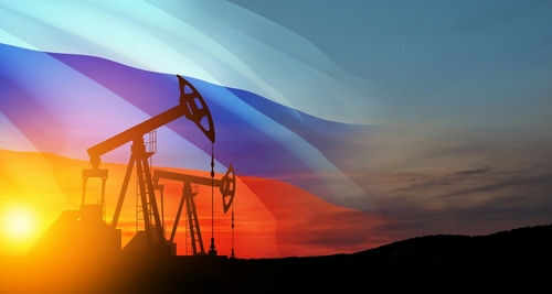 Oil pumps silhouetted against Russian flag and sunset.