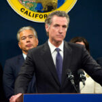 Phone Logs EXPOSE Newsom’s Office Lies Person speaks at podium with California seal behind.