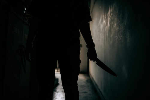 Silhouette of person holding knife in dark corridor