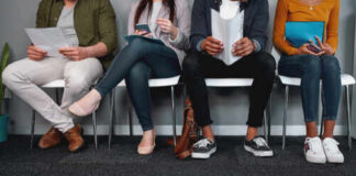 A diverse group of individuals sitting in a waiting room, each engaged with their devices or documents