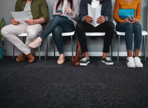 A diverse group of individuals sitting in a waiting room, each engaged with their devices or documents