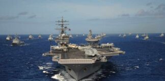 An aircraft carrier surrounded by various naval vessels in the ocean