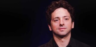 A man with curly hair smiling against a dark background
