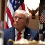 BETRAYAL: Ally Refused Access During Iran Strikes Man in suit sitting with flag background and eagle decoration