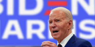 Man in suit speaking in front of blue background.
