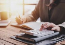 Person calculating taxes with a calculator and writing notes in a notebook at a desk
