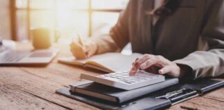 Person calculating taxes with a calculator and writing notes in a notebook at a desk
