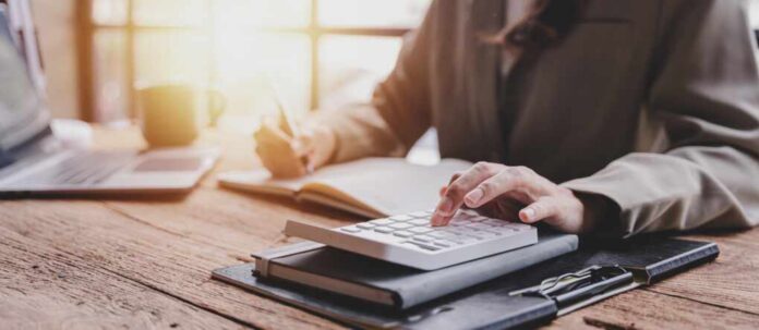 Person calculating taxes with a calculator and writing notes in a notebook at a desk