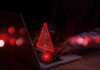 Red alert symbol over person typing on laptop
