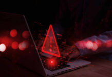 Red alert symbol over person typing on laptop