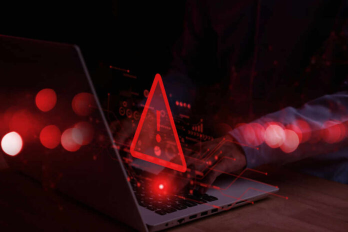 Red alert symbol over person typing on laptop