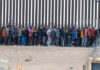 Large group of people standing near border fence