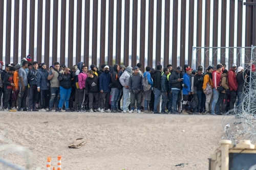 Large group of people standing near border fence