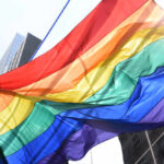 A vibrant rainbow flag waving against a city backdrop