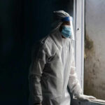 Record Evasion Scandal: Fauci Aide’s Shocking Indictment Healthcare worker in protective gear looking out of a window