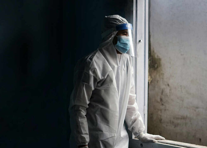 Healthcare worker in protective gear looking out of a window