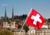 Swiss flag waving in front of historic buildings and church towers