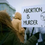 Person holding a sign that reads 'Abortion is Murder' at a protest