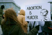 Person holding a sign that reads 'Abortion is Murder' at a protest