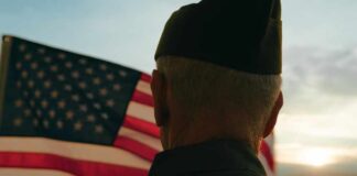 A veteran in uniform standing in front of an American flag at sunset