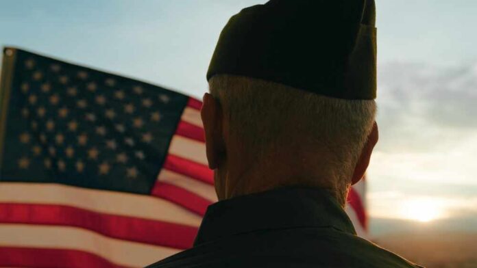 A veteran in uniform standing in front of an American flag at sunset