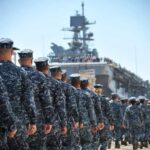 Navy personnel marching in formation towards a ship