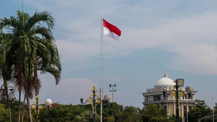 Indonesian flag waving in front of a building and palm trees