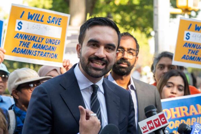 A man speaking at a rally with supporters holding protest signs