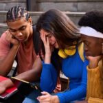 Universities Scramble: AI Disrupts Career Paths Three students sitting on steps, looking at a tablet with concerned expressions
