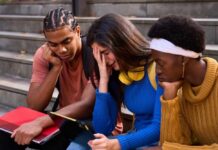 Three students sitting on steps, looking at a tablet with concerned expressions