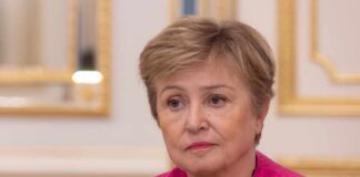 A woman in a pink jacket with a serious expression, seated in a formal interior