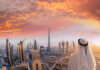 A person in traditional attire overlooking the Dubai skyline at sunset