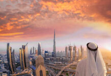 A person in traditional attire overlooking the Dubai skyline at sunset