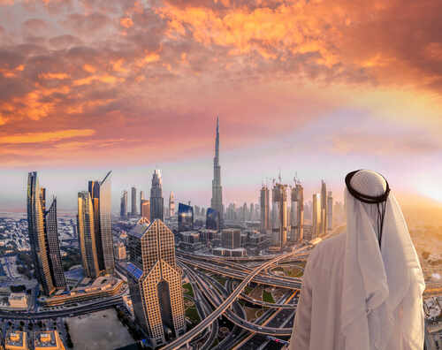 A person in traditional attire overlooking the Dubai skyline at sunset