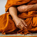 A close-up of a Buddhist monk's hand resting on orange robes during meditation