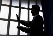 Silhouette of a person holding a book and raising a hand