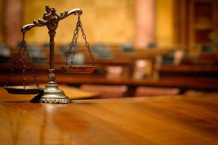 shutterstock_1166082523.jpg A close-up of a decorative scales of justice on a wooden table in a courtroom