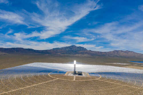 Aerial view of a solar power plant with a central tower and surrounding mirrors in a desert