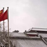 Two Chinese flags waving in the snow near traditional architecture
