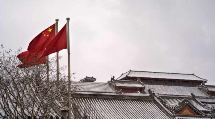 Two Chinese flags waving in the snow near traditional architecture