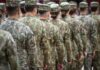 Explosive Revelations: Women’s War Fatalities Rise A soldier in uniform saluting in a military cemetery with white gravestones in the background