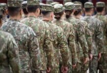 Explosive Revelations: Women’s War Fatalities Rise A soldier in uniform saluting in a military cemetery with white gravestones in the background