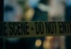 Caution tape marking a crime scene with blurred figures in the background