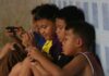 Group of children sitting against a wall, focused on their smartphones