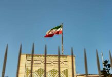 Iran Targets American Journalist: Alarming Plot Unveiled Iranian flag waving above a government building against a blue sky