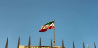 Iranian flag waving above a government building against a blue sky