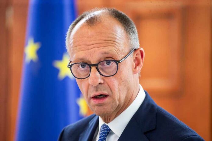 shutterstock_2670954973.jpg A man in a suit with glasses, looking serious in front of an EU flag