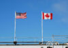 Canada’s Defense Spending Slammed — US Halts Board American and Canadian flags flying on poles against a clear blue sky