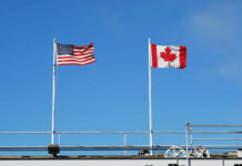 Canada’s Defense Spending Slammed — US Halts Board American and Canadian flags flying on poles against a clear blue sky