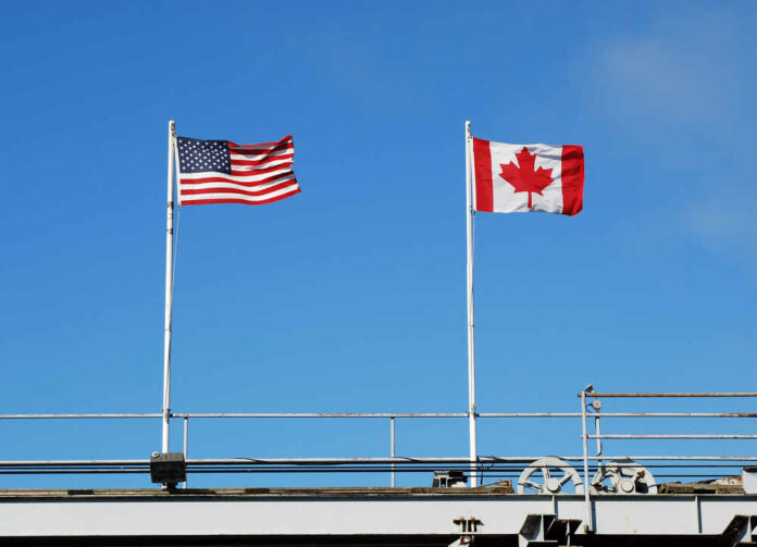 Flags,Flying,At,A,Us,And,Canadian,Border American and Canadian flags flying on poles against a clear blue sky